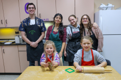 Baking class in a kitchen with adults and children posing for a picture.
