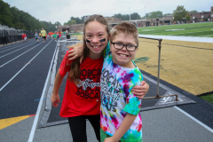 Two people posing in a stadium, one wearing red shirt and the other in tie-dye.
