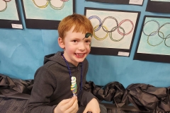 Young boy sitting in front of a display of olympic rings posters on a blue wall.
