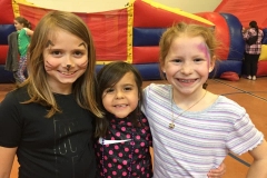 Three children posing in front of an inflatable bounce house at a carnival.