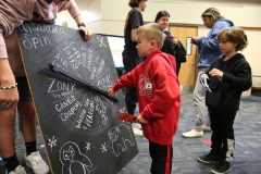 Children playing with a chalkboard sign at a school event.