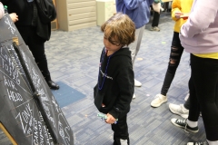Children gathered around a chalkboard with writing on it.