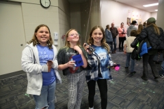 Three girls in a school gymnasium holding balloons and smiling at camera.