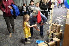 In a bustling airport lobby, a man and a child are interacting with colorful luggage tags on display.