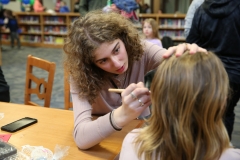 Woman applying makeup to woman's face at table in room.