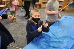 Children at a table in a library, creating crafts using construction paper and markers.