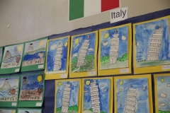 Artwork displayed on a wall featuring children's drawings of towers and scenes with the title "Italy" at top.