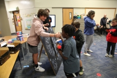 People gathered around a table with a chalkboard, engaging in an activity.