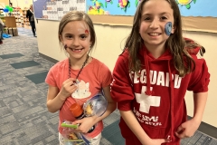 Two young girls posing in a classroom setting, one wearing a red hoodie with "SECARE" written on it and the other in a white
