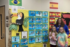 This is a photograph of a classroom display board featuring various colorful artwork, including paintings of birds and fish,