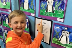 Boy in front of a wall of children's artwork at an art exhibition.