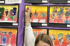 Young girl posing in front of a display of children's art on a purple wall.