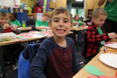 Boy sitting at desk in classroom with paper plate on table.