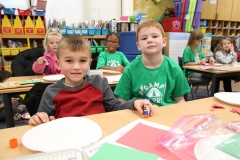 Two boys sitting at a table in a classroom, smiling and looking at the camera.