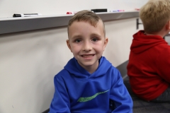 Young boy in blue jacket sitting at desk.