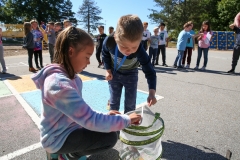 Two children in a parking lot near a butterfly. A child is holding a butterfly on a stick.