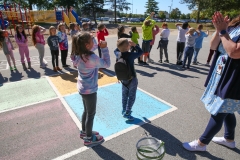 Children in a schoolyard, participating in an outdoor activity led by an adult.