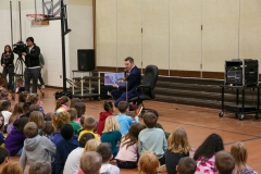 Man reading a book to children in classroom setting.