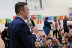 Man in suit speaking at podium to crowd of people.