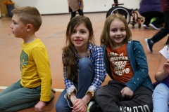 Two children sitting on floor in gymnasium, smiling at camera.