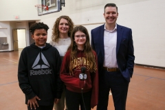 A group of people posing for a picture in a gymnasium, with one person standing behind them.