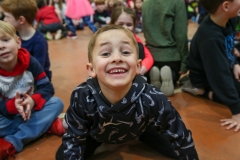 Boy in camo pajamas on floor smiling at camera.