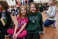 Two young girls sitting on the floor in a school gymnasium.