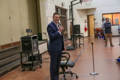 Man in suit speaking at podium in gymnasium.