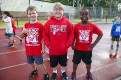 Three children in red shirts standing on a track at a walkathon event.