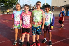 Four children in colorful tie-dye shirts posing for a picture at a track.