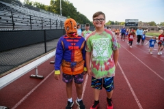 Two people standing on track at night. One person wearing a colorful costume and another in casual clothes. Both are smiling.