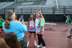 Two girls posing in front of a stadium, one holding a camera, both smiling for the photo.