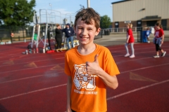 Boy in orange shirt giving thumbs up at track.