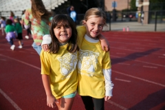 Two young girls posing together in yellow shirts, smiling at the camera, on a field during a walkathon event.