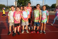Group of children in colorful tie-dye shirts posing for a picture on a track.
