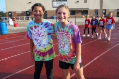Two young people posing for a picture at an event, both wearing tie-dye shirts and standing on a track.