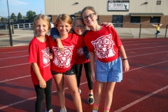 Four girls in red shirts standing on a track, smiling at the camera.