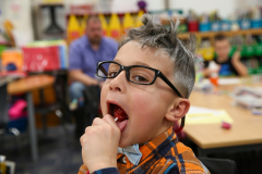 Little boy in glasses licking a tootsie pop.