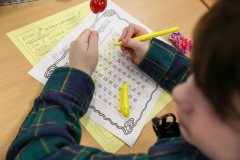 Child sitting at a table working on a worksheet with a lollipop.