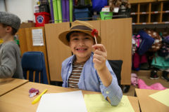 Young boy in a classroom holding a red lollipop.