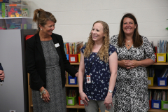 Three women in a library, two standing and one sitting, posing for a picture. One woman is smiling at the camera, while