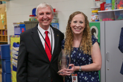 An older man and woman posing together at an event, both smiling, with the woman holding a glass plaque that reads "Sherri