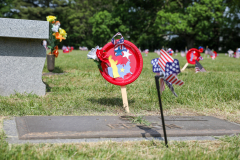 Memorial grave site with small American flags, a wreath, and a red, white, and blue ribbon on a pole.