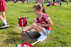 Little girl in red jersey crouching by a grave marker, holding a small flag and flowers.