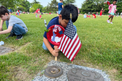 Young boy holding an american flag in front of a grave marker.