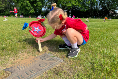 Little girl holding a flag while looking at a grave.