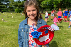 Girl in patriotic shirt standing in front of grave decorated with American flags.
