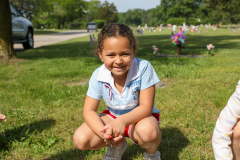 Girl in blue shirt kneeling on grass near graves.