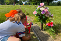 Two people standing near a grave with flowers on it.