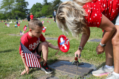 Woman placing a flag on a grave. Child looking at the flag. Both are standing in front of a grave.